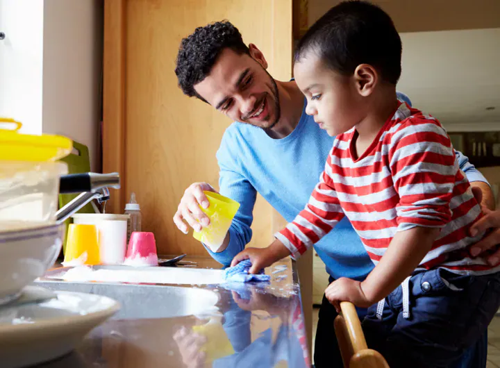 A young child is helping his father wash the dishes in a soapy sink