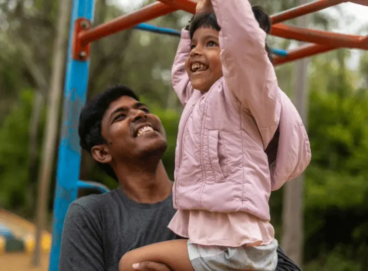 A loving father spends quality time with his happy daughter, helping her at the monkey bars.