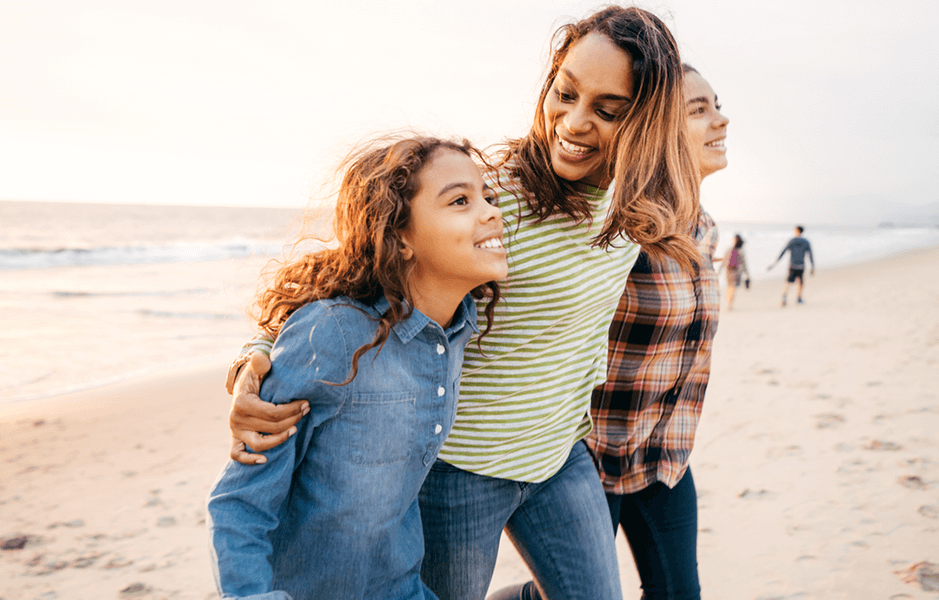 A mum and her two daughters look hopeful as they walk along the beach at sunset.