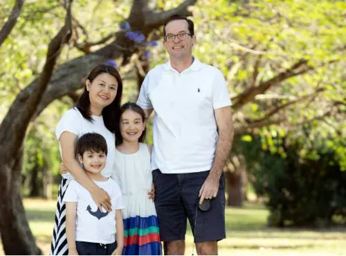 A family of four are standing close together, smiling, in a park