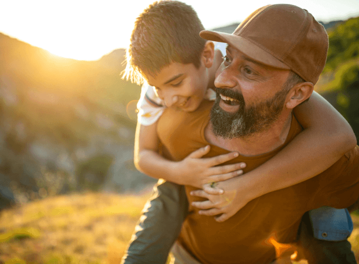 A dad is piggybacking his son, they are smiling together.