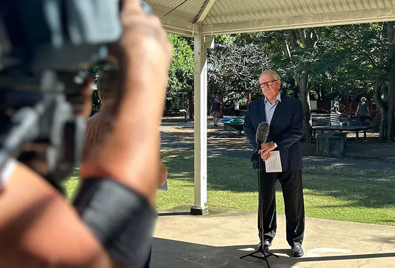 Professor Matt Sanders stand in front of a microphone at a park, while a camera records him.