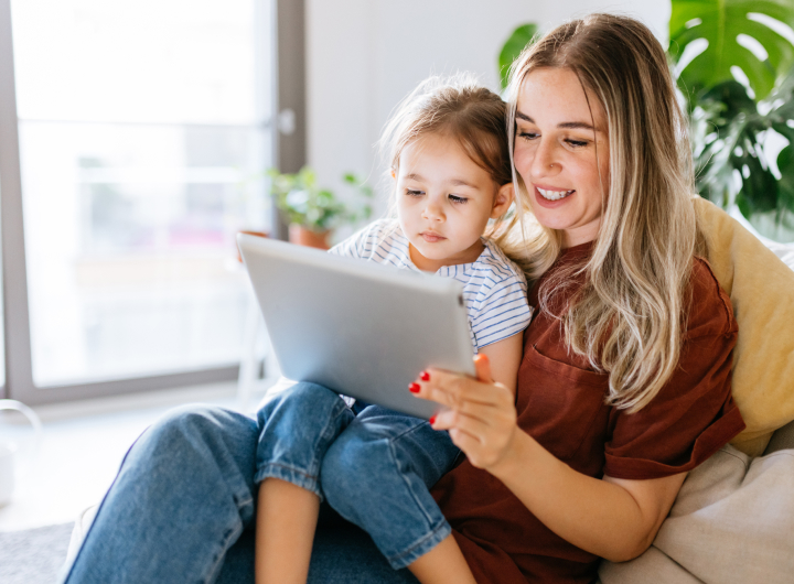 A young girl sits on her mum’s lap, watching screens together can help with iPad tantrums