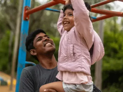 A loving father spends quality time with his happy daughter, helping her at the monkey bars.