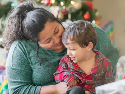 A mother and young son smiling together in front of holiday decorations