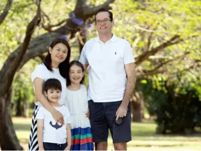 A family of four are standing close together, smiling, in a park