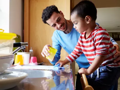 A young child is helping his father wash the dishes in a soapy sink