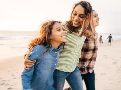 A mum and her two daughters look hopeful as they walk along the beach at sunset.