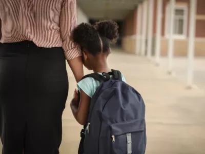 A child worried about friendships clings to her mother as they walk into school