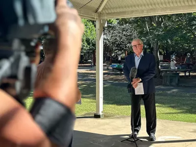 Professor Matt Sanders stand in front of a microphone at a park, while a camera records him.